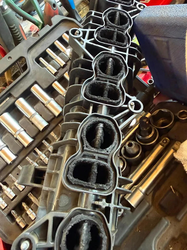 Dismounted plastic intake manifold with thick soot and carbon deposits.